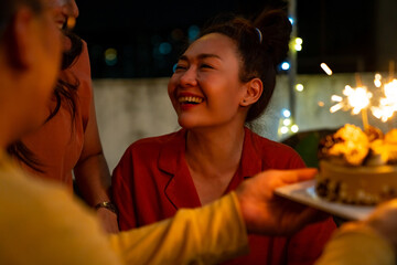 Diversity Asian millennial people friends enjoy celebration birthday party together at outdoor rooftop with food and drink. Woman excited with birthday cake and blowing birthday candle with happiness