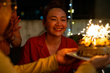 Diversity Asian millennial people friends enjoy celebration birthday party together at outdoor rooftop with food and drink. Woman excited with birthday cake and blowing birthday candle with happiness