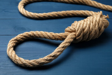 Rope noose with knot on blue wooden table, closeup