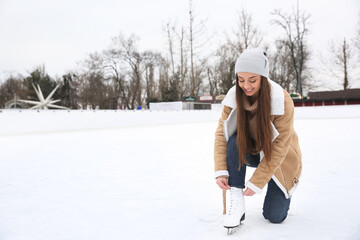 Woman lacing figure skate on ice rink. Space for text