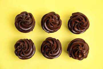Delicious chocolate cupcakes with cream on yellow background, flat lay