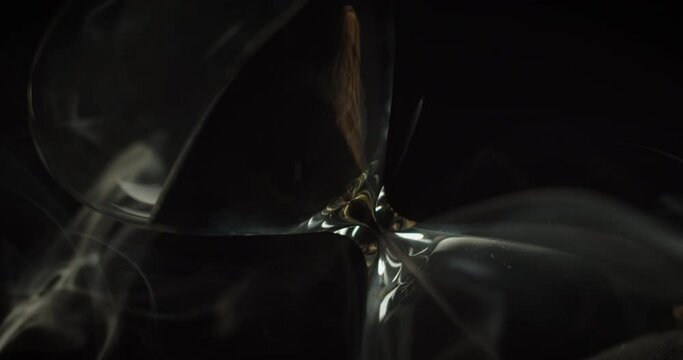 An hourglass slowly rotating while white smoke surrounding it. Abstract running time concept. 