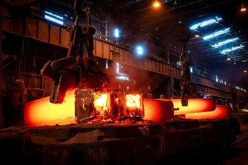 The grapple lifts a large, hot metal forging