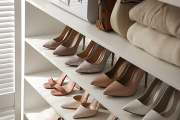 Fototapeta na wymiar Stylish women's shoes, clothes and bags on shelving unit in dressing room