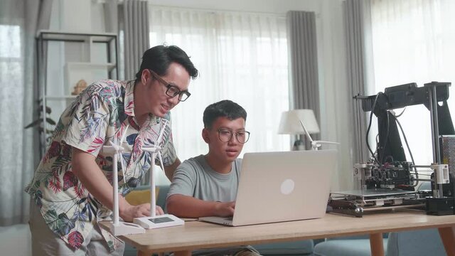 Cheerful Father And His Son Using Laptop Computer Programming Electric Wind Turbine Model And 3D Printer At Home
