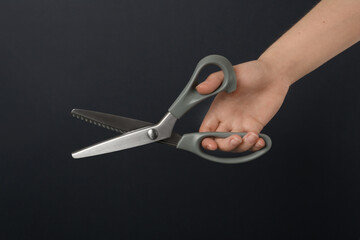 Woman holding sewing scissors on black background, closeup