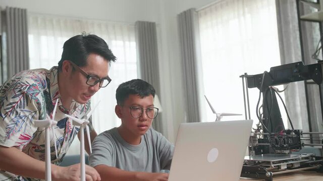 Father Teach His Son Using Laptop Computer Programming Electric Wind Turbine Model And 3D Printer At Home
