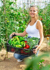 Happy woman gardener holding basket with fresh vegetables in garden