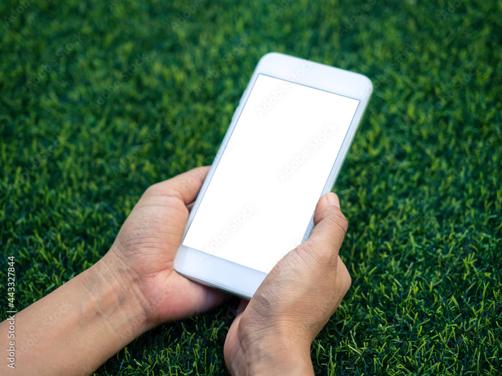 Poster mockup image of phone. close-up white blank screen on mobile phone in hands on green artificial gras