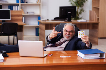 Old male employee playing cards at workplace