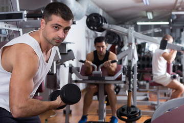 Muscular young man doing exercises with dumbbells at gym