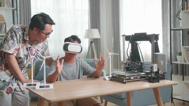 Asian Father Teach His Son While Wearing Vr Glasses With Electric Wind Turbine Model And 3D Printer At Home
