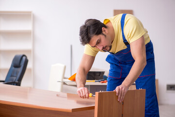 Fototapeta na wymiar Young male carpenter repairing desk in the office