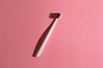 white toothbrush with black charcoal infused bristles on pink background, top view