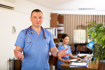 Obraz premium Positive adult male doctor in uniform standing in medical office