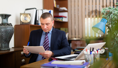 Concentrated young adult businessman working with documents at workplace in office