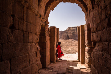 A lonely woman in red staring at the desert mountains of the site of Petra. Petra is  an...