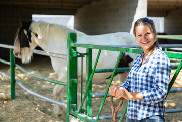 Portrait of successful woman farmer engaged in breeding of horses standing near outdoor enclosure