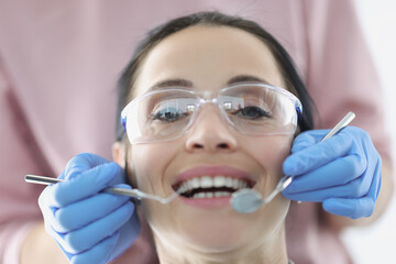 Dentist examining oral cavity of female patient wearing safety glasses in clinic