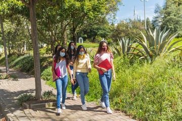 A group of Latina teenage friends walk to class wearing masks as a prevention against Coronavirus. Education and health concept