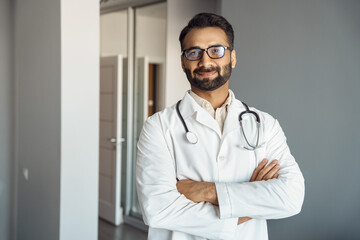 Portrait of male doctor wearing white lab coat, stethoscope standing and looking at camera in clinic hall. Arabian indian therapist, general practitioner headshot. Medicine, heal insurance, healthcare - Powered by Adobe