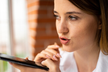 close-up of a girl holding a phone near her face and recording a voice message talking on a speakerphone on the Internet. Voice or virtual assistant on your mobile phone.