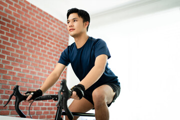 Plakat Asian man cycling a bicycle on a trainer in the house.