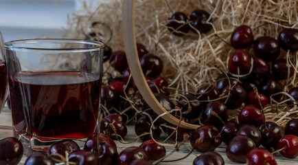 Cherry and cherry juice or wine on a wooden table, a decanter and a glass with juice, a basket with...