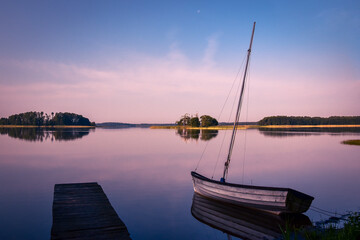 Old sailboat and wooden jetty situated on the shore of the lake, in the evening sun