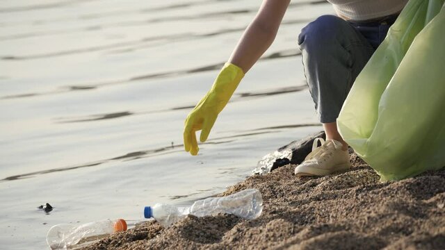 A woman cleans up trash at the lake. Young woman puts empty plastic bottles in a trash bag. Close-up, 4K UHD.
