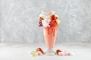 Extreme milkshake. Freakshake. Pink strawberry monstershake with sweets on grey background.  Overshake