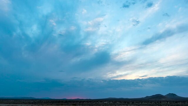 A flash of pink on the horizon signals the dawn of a new day at sunrise in the Mojave Desert - aerial time lapse