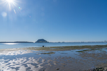 Dinghy lies on sand at low tide with Mount Maunganui on horizon.