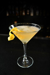iced yellow lemon fruit juice cocktail or mocktail with lemon peel in glass goblet on black marble bar counter dark night background cold alcohol drink menu