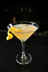 iced yellow lemon fruit juice cocktail or mocktail with lemon peel in glass goblet on black marble bar counter dark night background cold alcohol drink menu