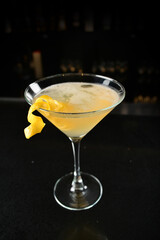 iced yellow lemon fruit juice cocktail or mocktail with lemon peel in glass goblet on black marble bar counter dark night background cold alcohol drink menu