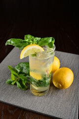 iced basil lemon mint leaf cooler mocktail / kombucha in glass on bar counter dark night background cold halal drink menu