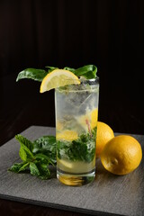 iced basil lemon mint leaf cooler mocktail / kombucha in glass on bar counter dark night background cold halal drink menu