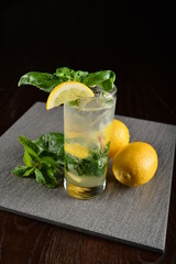 iced basil lemon mint leaf cooler mocktail / kombucha in glass on bar counter dark night background cold halal drink menu