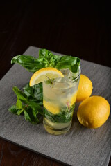iced basil lemon mint leaf cooler mocktail / kombucha in glass on bar counter dark night background cold halal drink menu