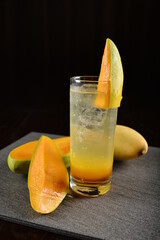 iced Thai mango fruit mocktail with soda kombucha in glass on bar counter dark night background...