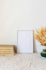 Home decor mock-up, blank picture frame near white painted concrete wall ,vase with dried yellow oat stalks, old books