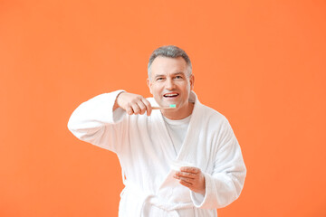 Mature man brushing teeth on color background