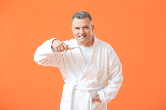 Mature man brushing teeth on color background