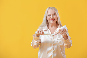 Mature woman brushing teeth on color background