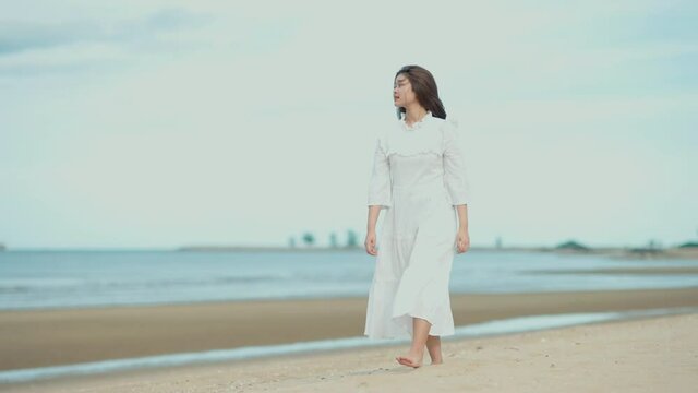 Cute Asian girl walking on the beach by the beach. She turned to smile at the camera. On a day with clear skies, good weather, 4k resolution.