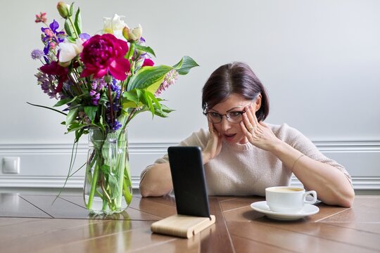 Surprised emotional mature woman looking at smartphone screen