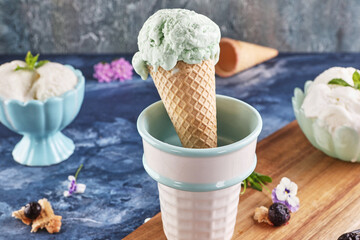 Fototapeta na wymiar Still life with pistachio and creamy ice cream in vases and cone on blue background