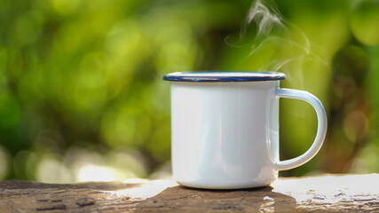 white enamel coffee mug on the old wooden table green forest bokeh background