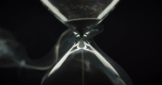 Beautiful smoke surrounding an hourglass with black sand. End of time cycle. 